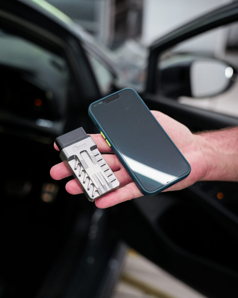 PDM und Smartphone in der Hand am geöffneten Fahrzeug